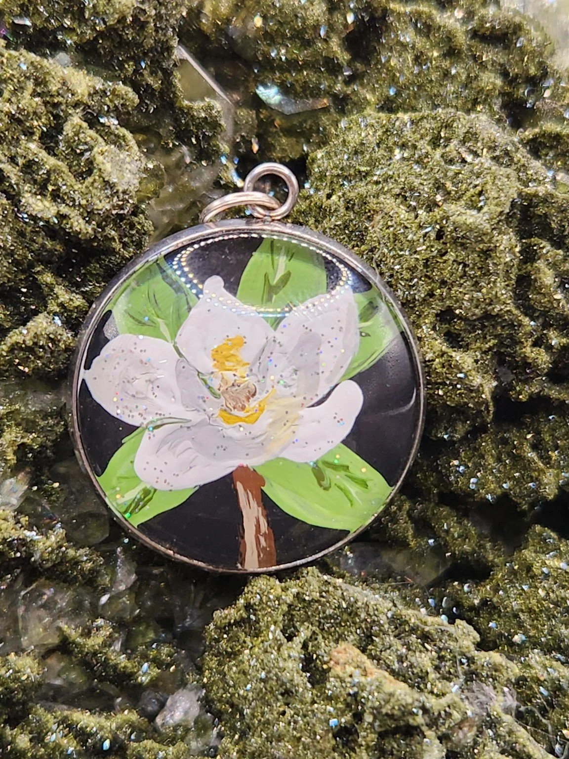 Magnolia flower art pendant displayed among green crystals. Crystal display and props not included.