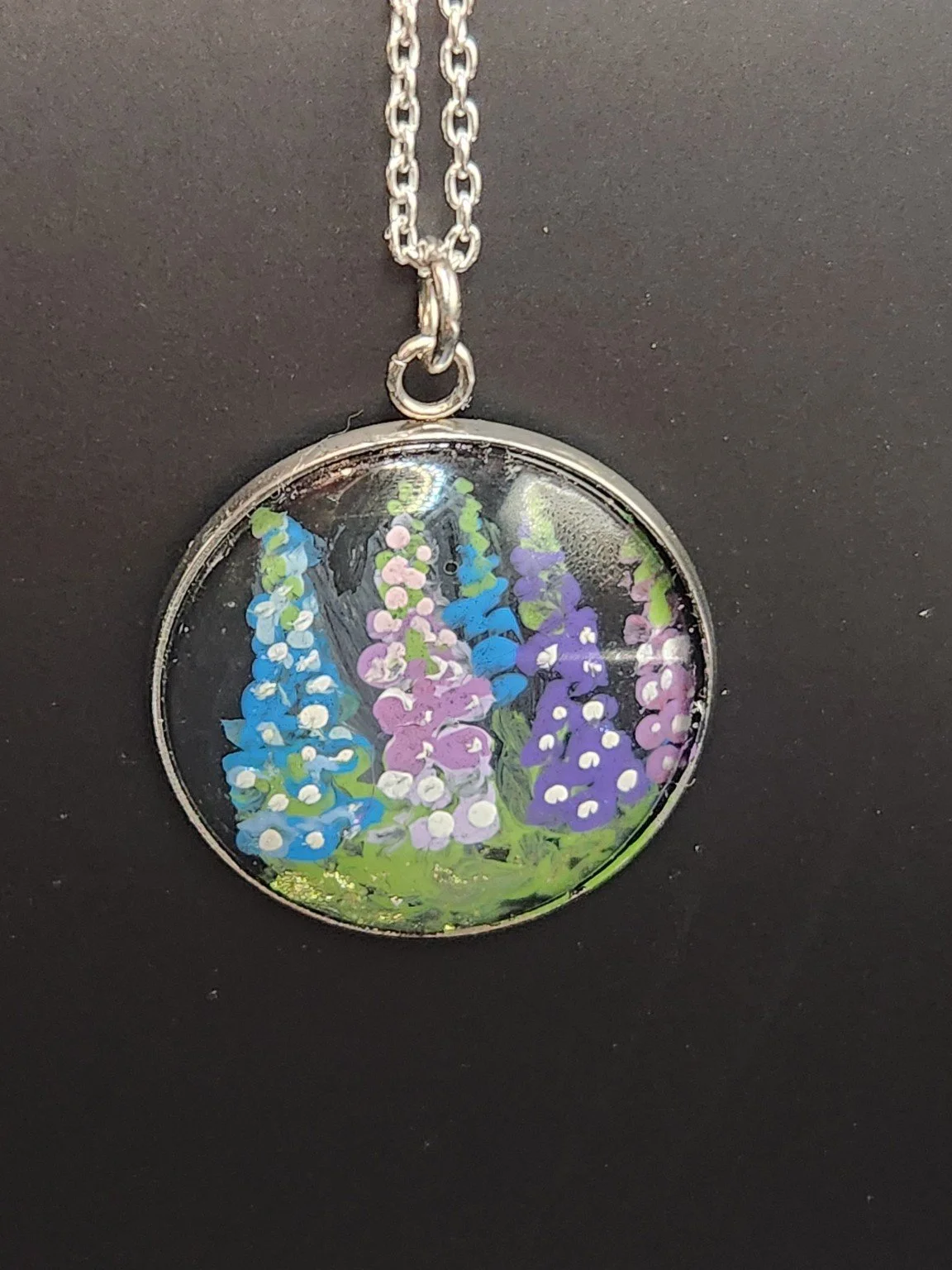 Colorful delphinium flower art pendant shown on a silver-tone chain against a dark background. Chain not included.