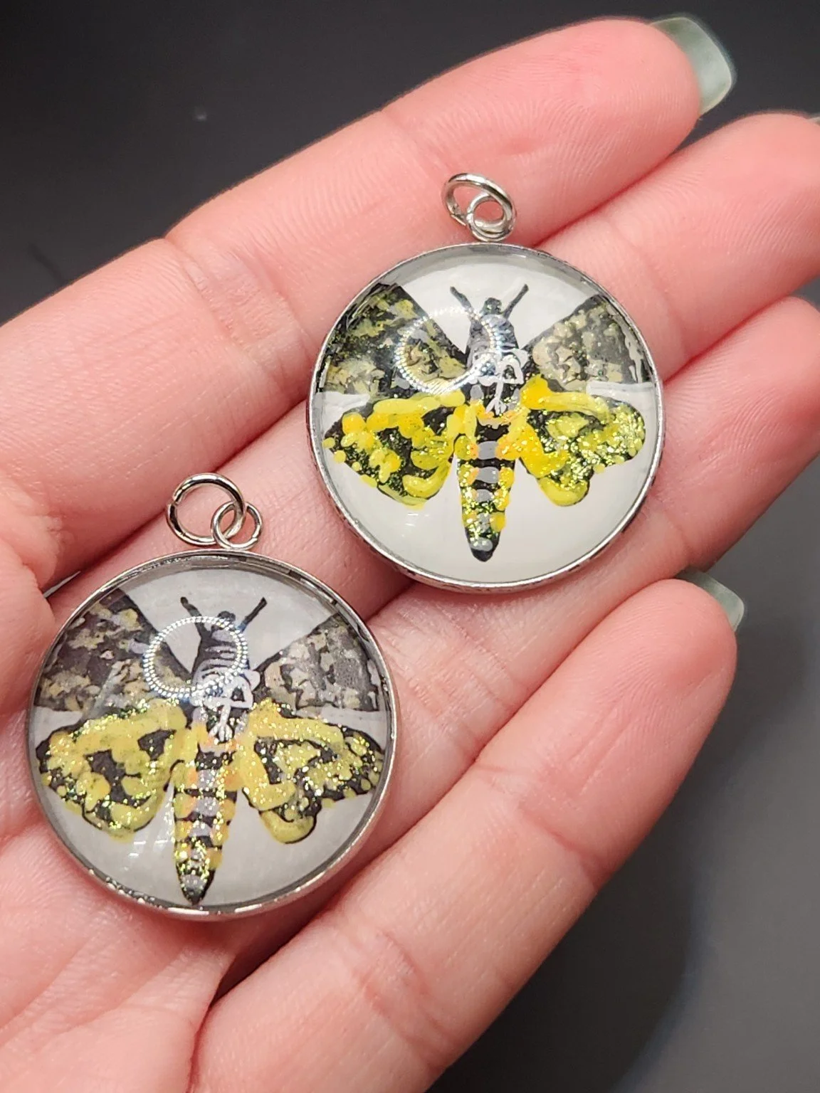 Death’s-head moth pendant comparison held in a hand: the hand-painted original is at the top right, and the printed reproduction is at the bottom left.