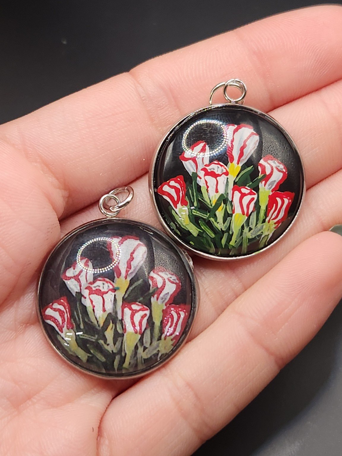 Two candy cane sorrel pendants held in a hand: hand-painted original at the top right and printed reproduction at the bottom left.