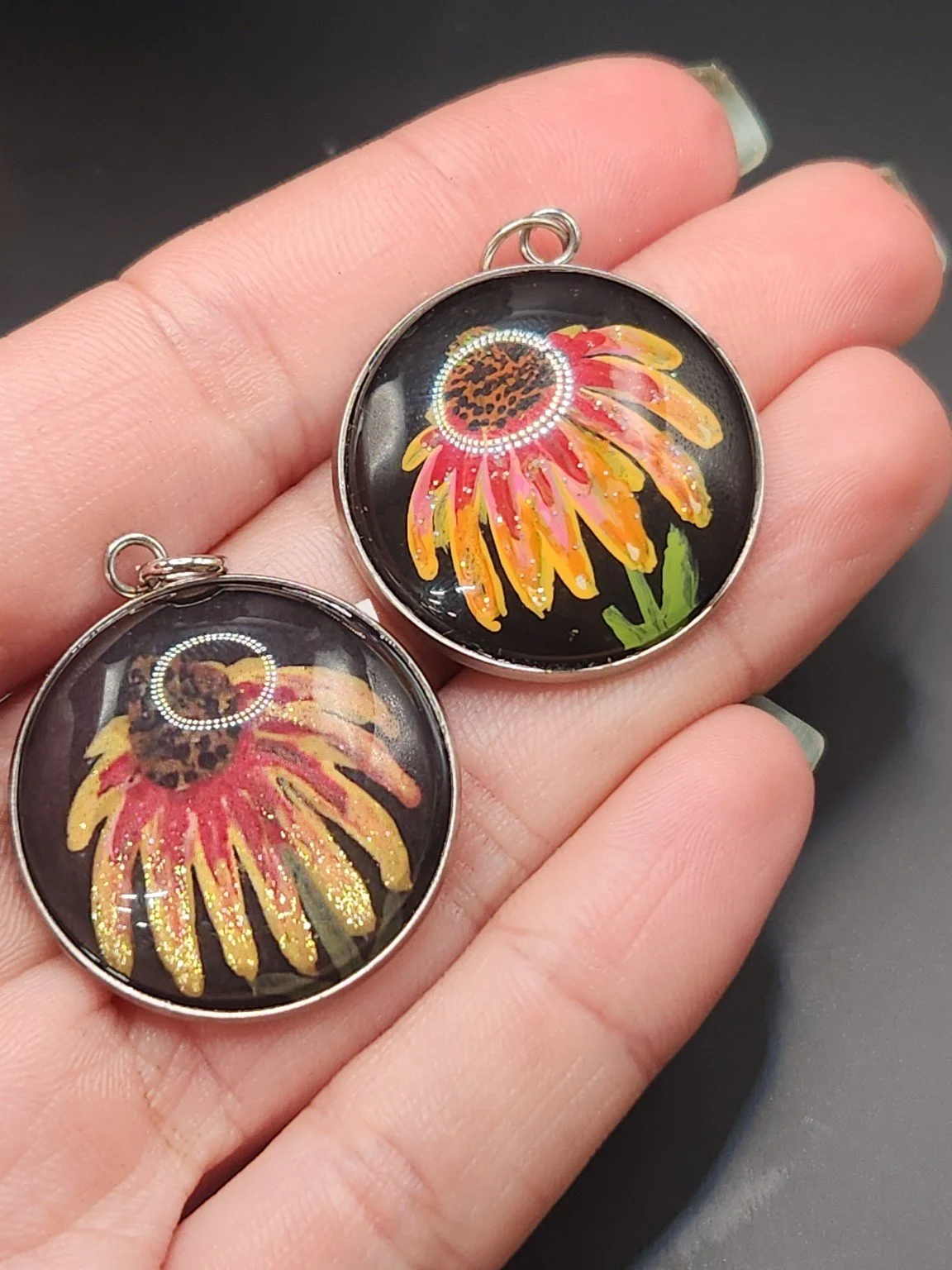 Coneflower pendant comparison held in a hand: the hand-painted original is at the top right, and the printed reproduction is at the bottom left.