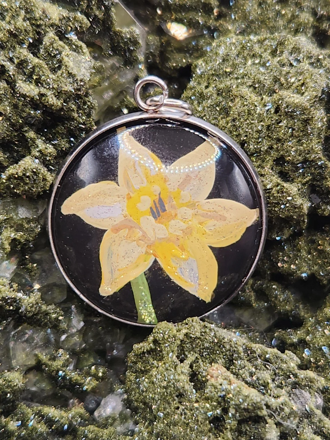 Yellow daffodil flower art pendant nestled in a sparkling green crystal display. Crystal and display props not included.
