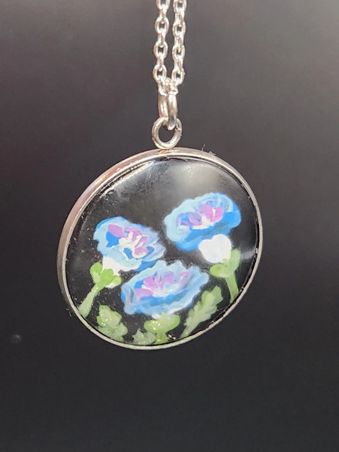 Blue morning glory art pendant hanging from a silver-tone chain against a dark background. Chain not included.