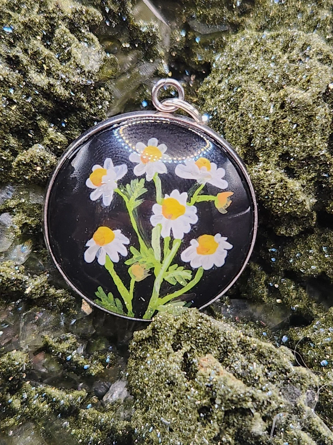 Chamomile flower art pendant resting on a green crystal display. Crystal display not included.