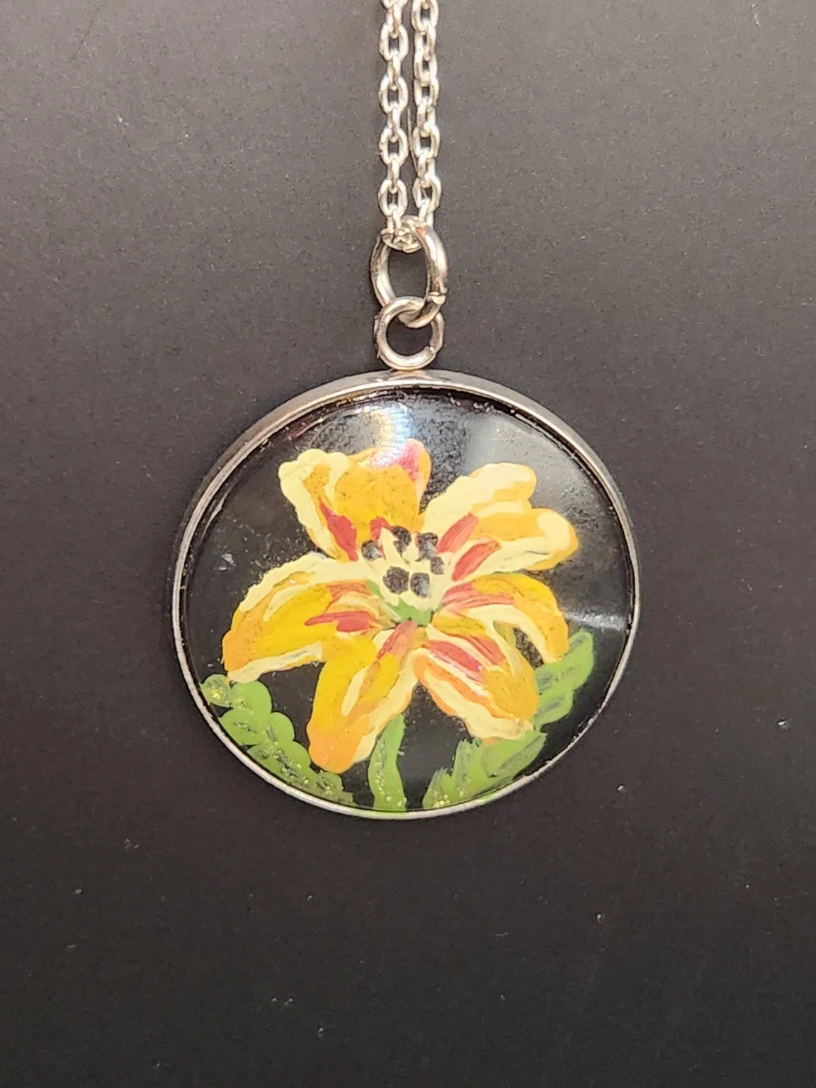 Yellow and orange daylily flower art pendant hanging from a silver-tone chain. Chain not included.