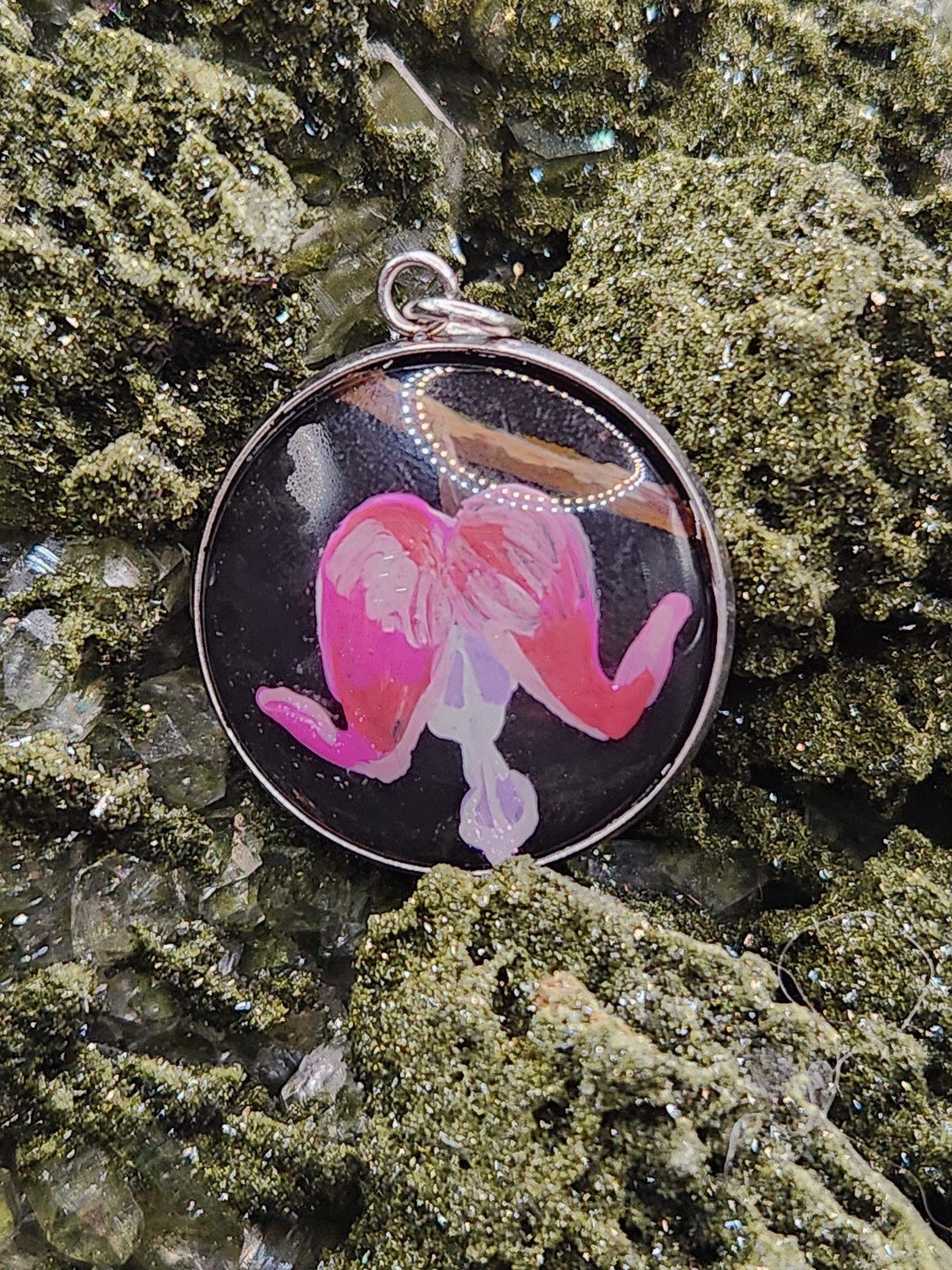Bleeding heart flower art pendant displayed among green crystals. Crystal display and styling props not included.