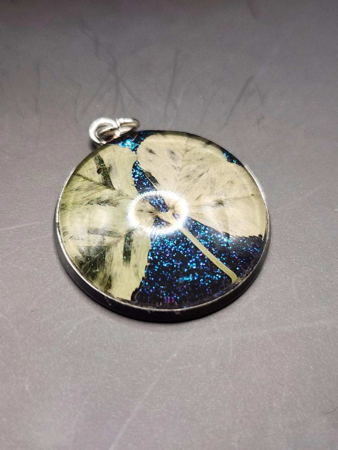 Naturally Unique N003: real pressed four-leaf clover pendant with blue glitter background, close-up on gray.