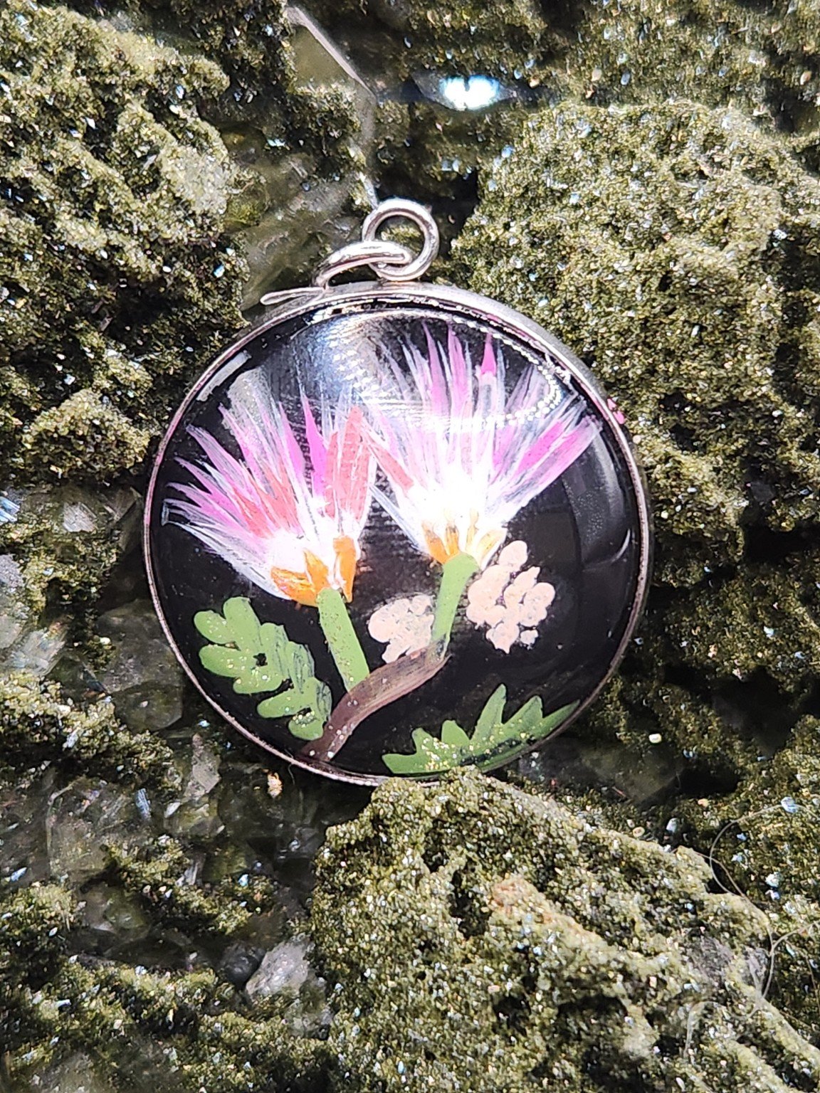Pink mimosa flower art pendant resting on a green crystal display. Crystal display not included.
