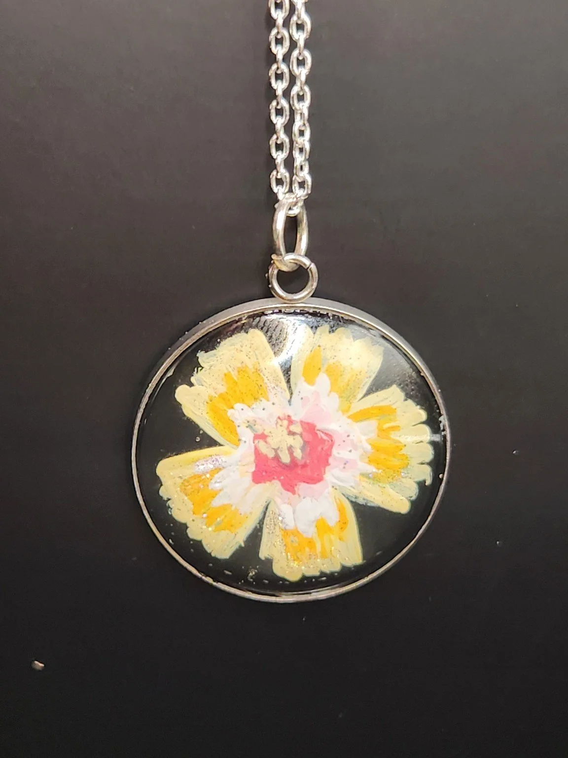 Yellow hibiscus flower art pendant shown on a silver-tone chain against a dark background. Chain not included.