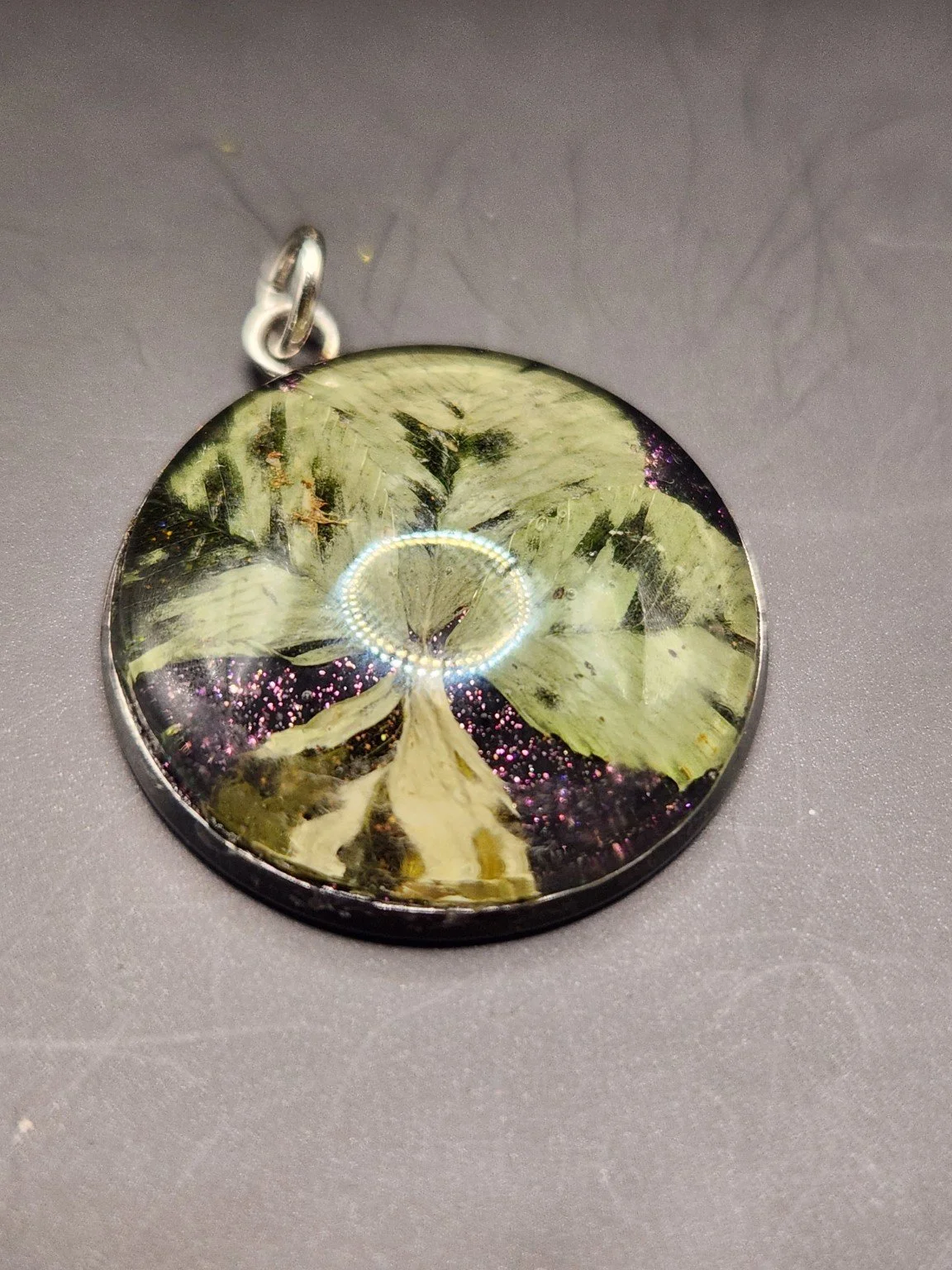 Perfectly Imperfect I003: real four-leaf clover pendant with purple glitter and irregular translucent leaf patterns, close-up on gray.