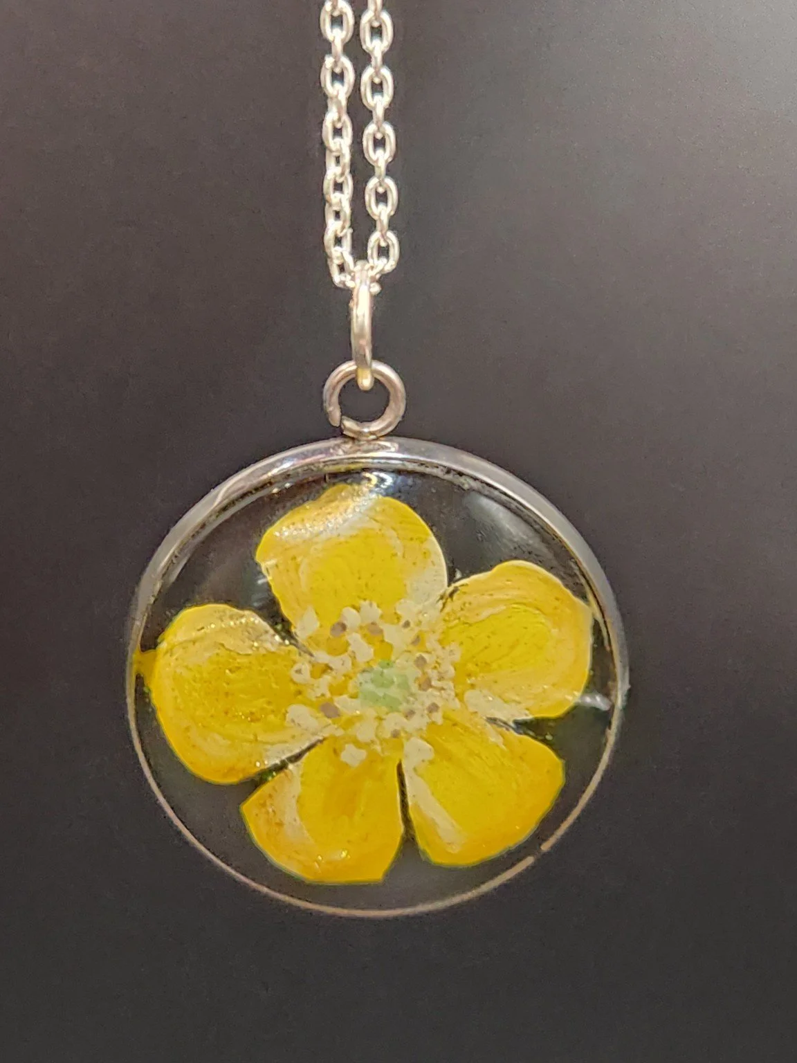 Golden yellow buttercup flower art pendant hanging from a silver-tone chain against a dark background. Chain not included.