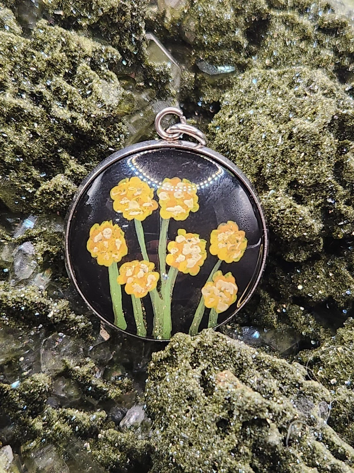 Billy button flower art pendant displayed among green crystals. Crystal display and styling props not included.