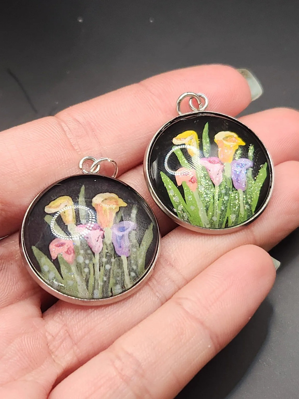 Calla lilies pendant comparison held in a hand: the hand-painted original is at the top right, and the printed reproduction is at the bottom left.