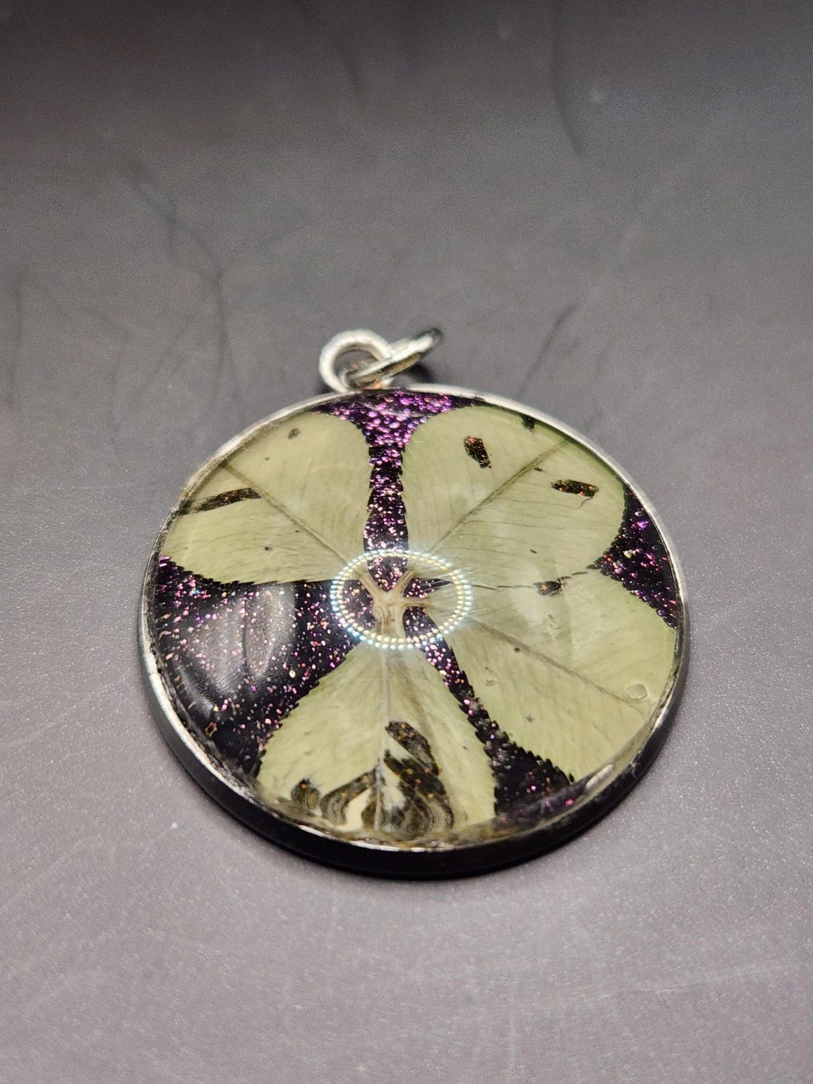 Pristine P003: real pressed four-leaf clover pendant with purple glitter background, close-up on gray.
