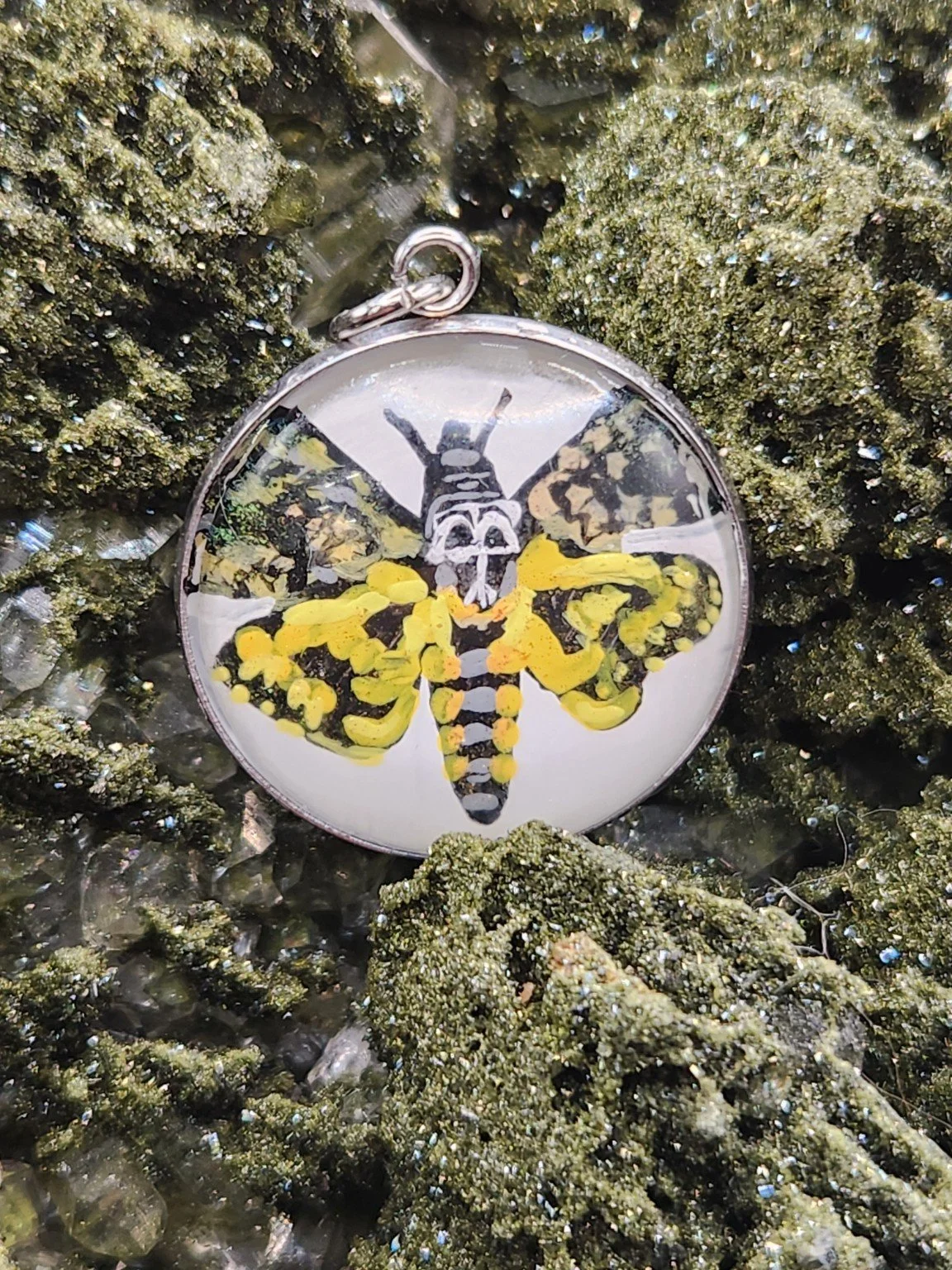 Death’s-head moth art pendant resting on a green crystal display. Crystal display not included.
