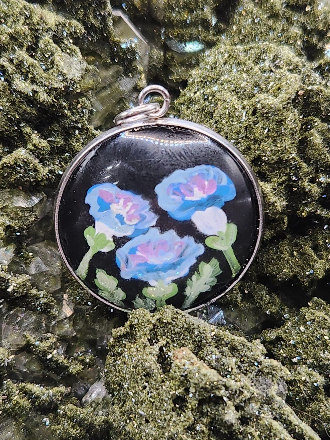 Blue morning glory art pendant nestled in a sparkling green crystal display. Crystal and display props not included.