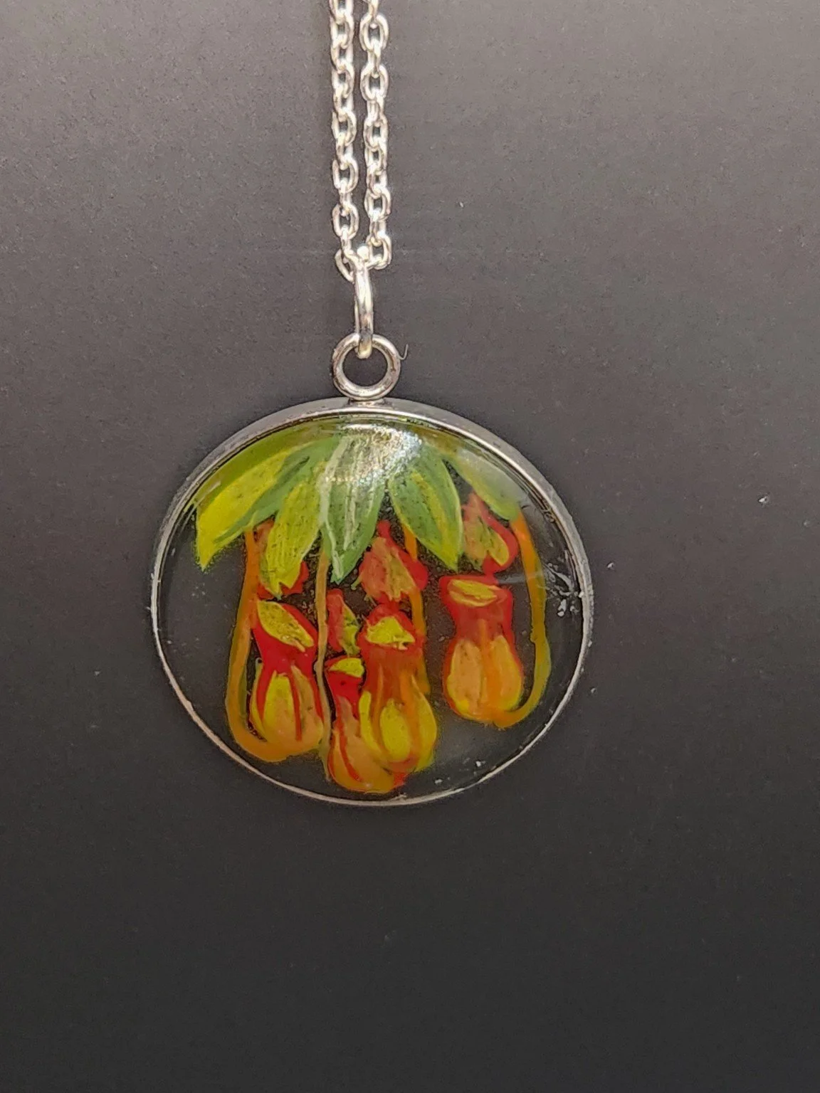 Pitcher plant art pendant shown on a silver-tone chain against a dark background. Chain not included.