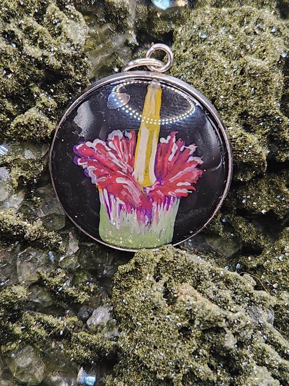 Corpse flower art pendant resting on a green crystal display. Crystal display not included.