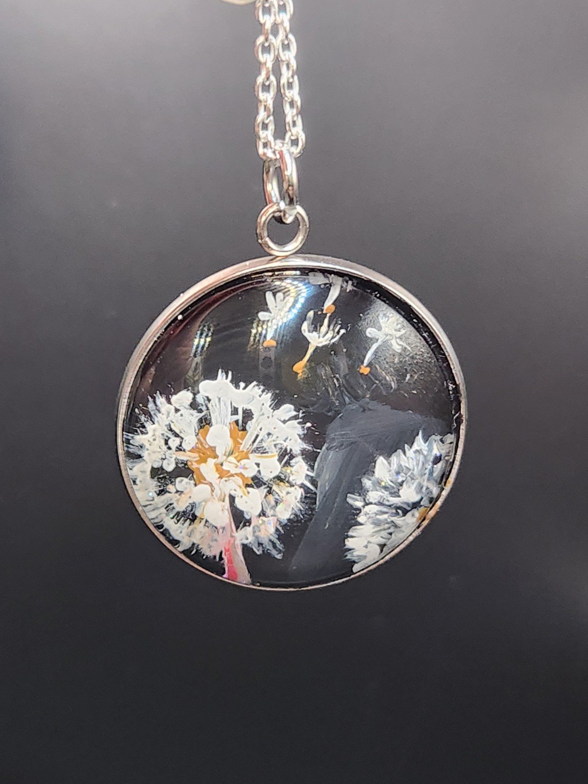 Dandelion Wish art pendant with white seed heads hanging from a silver-tone chain against a dark background. Chain not included.