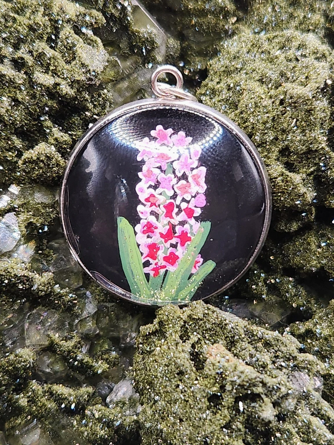 Pink hyacinth flower art pendant nestled in a sparkling green crystal display. Crystal and display props not included.