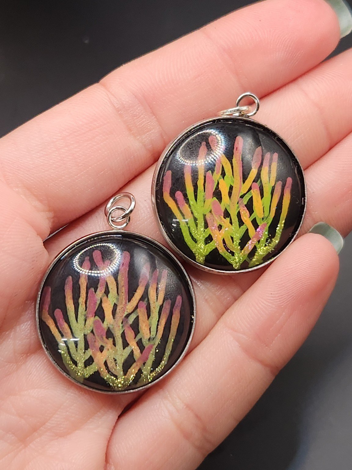 Two firestick cactus pendants held in a hand: hand-painted original at the top right and printed reproduction at the bottom left.