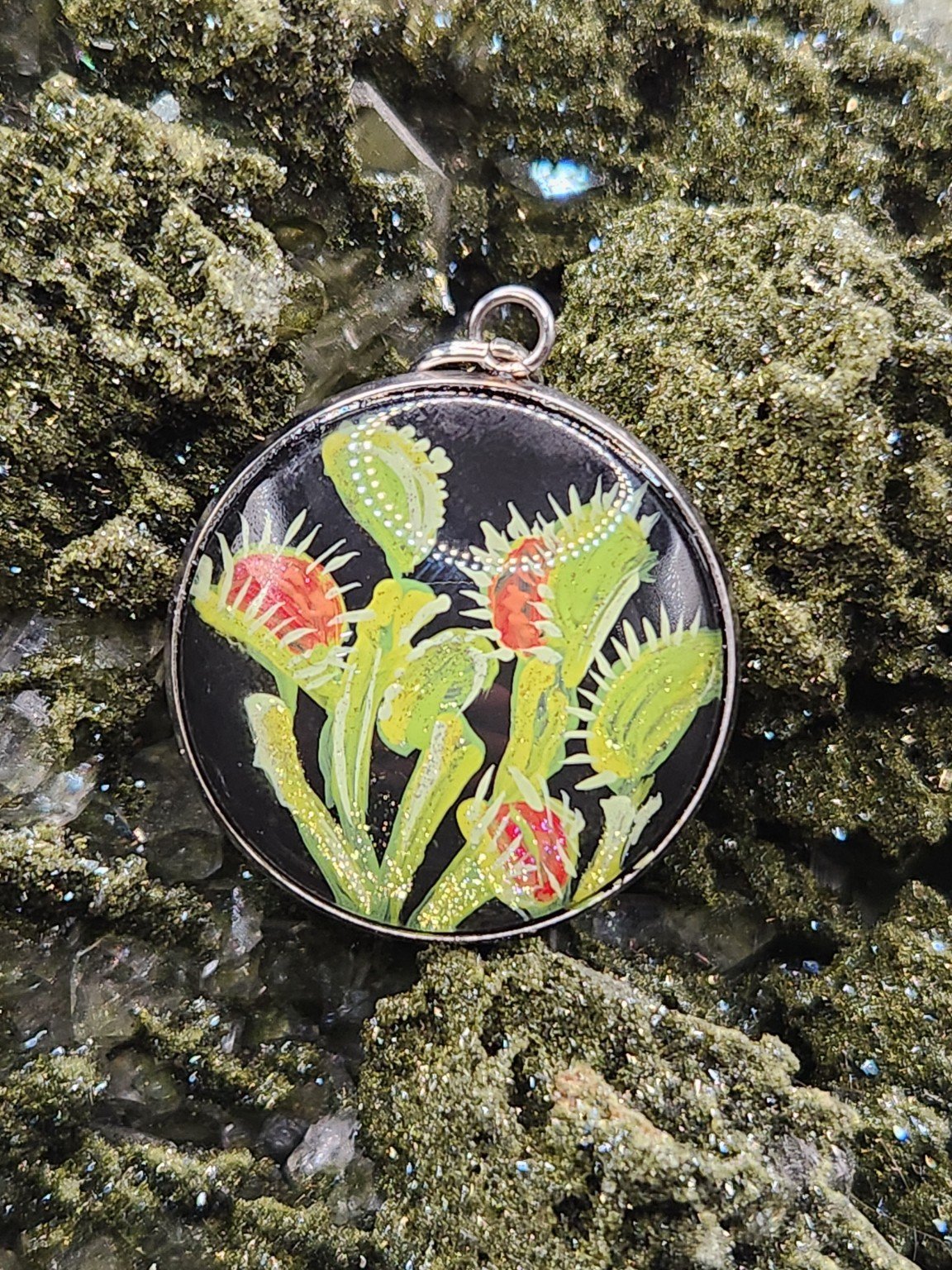 Green and red Venus flytrap art pendant nestled in a sparkling green crystal display. Crystal and display props not included.
