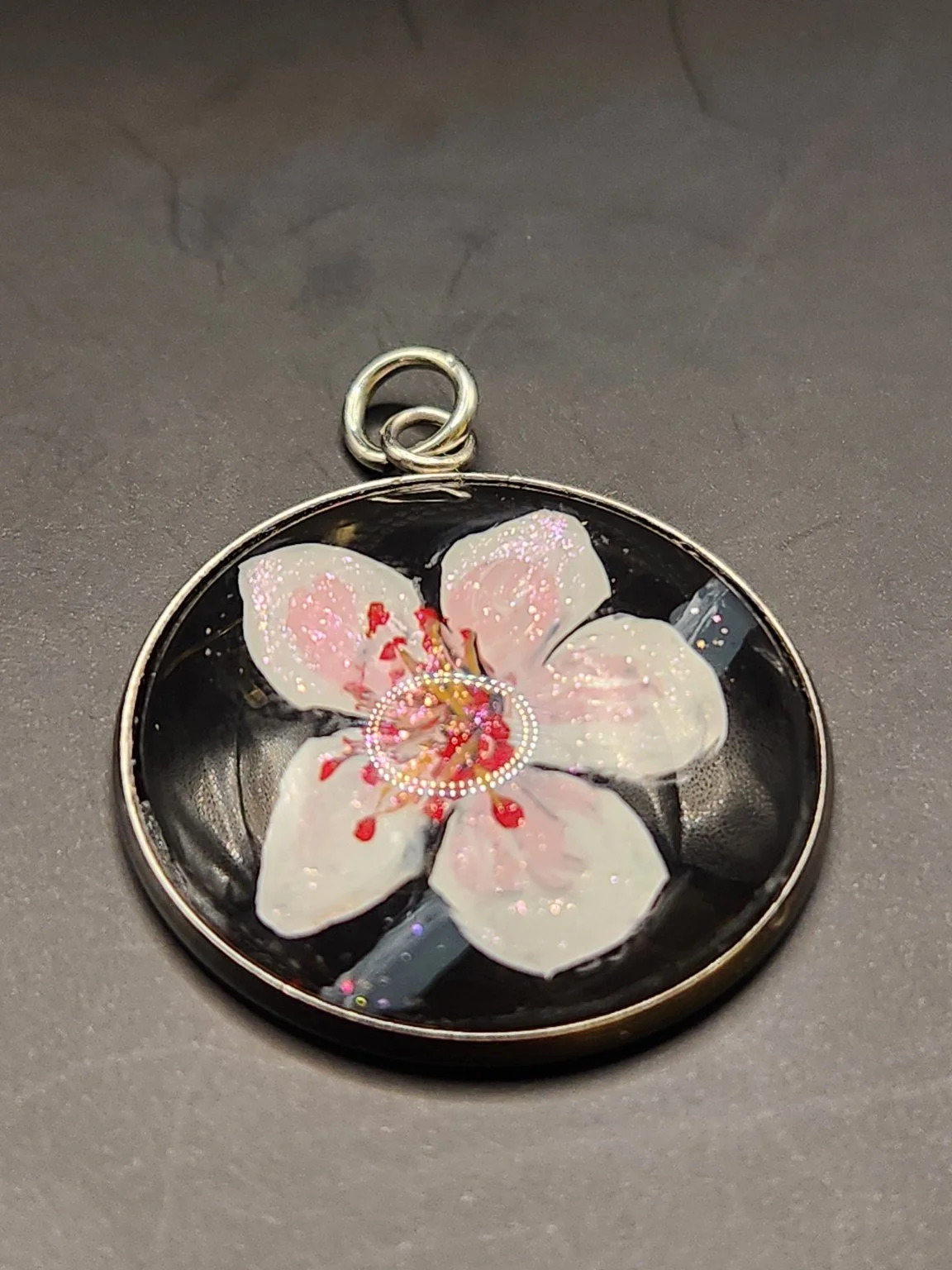 Pink cherry blossom flower art pendant with glitter accents in a silver-tone bezel.