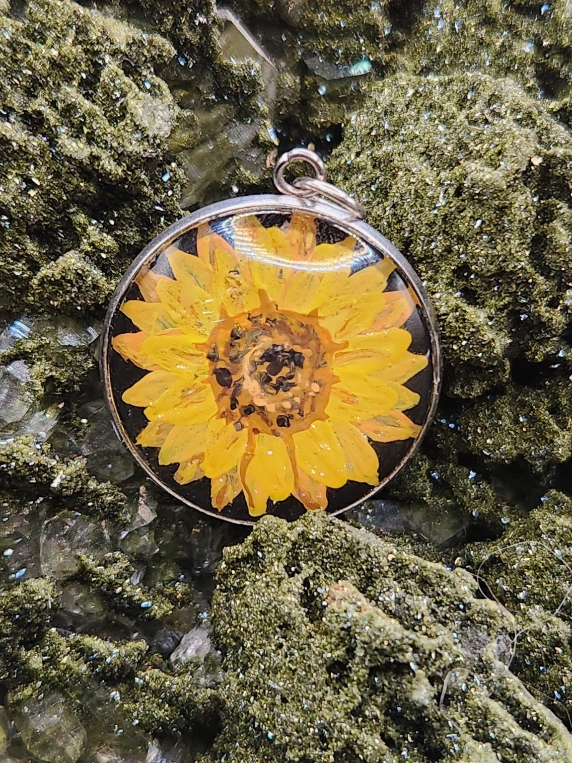Yellow sunflower art pendant displayed among green crystals. Crystal display and styling props not included.