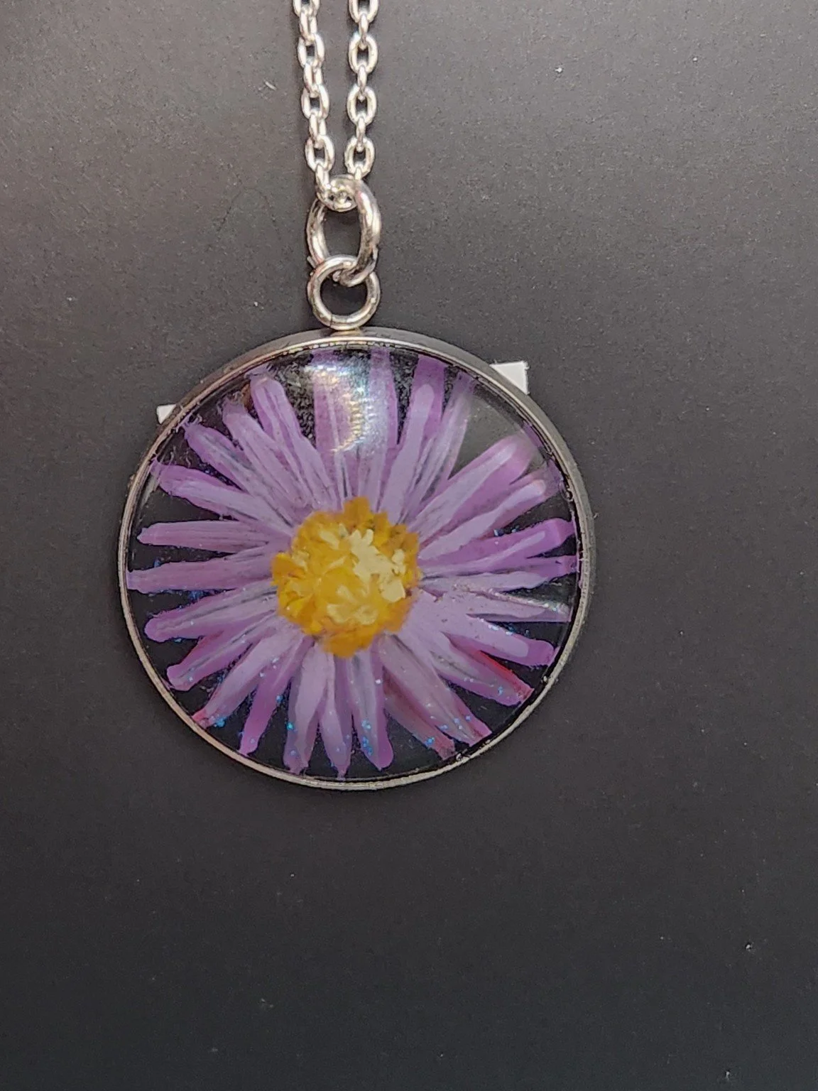 Purple daisy flower art pendant hanging from a silver-tone chain. Chain not included.