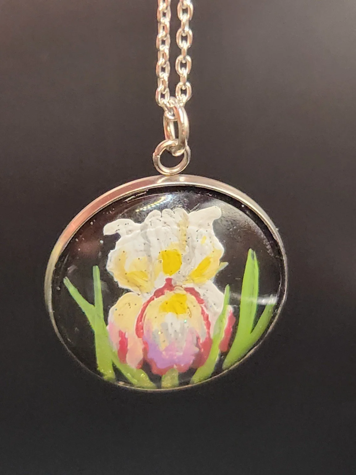 Iris flower art pendant hanging from a silver-tone chain against a dark background. Chain not included.