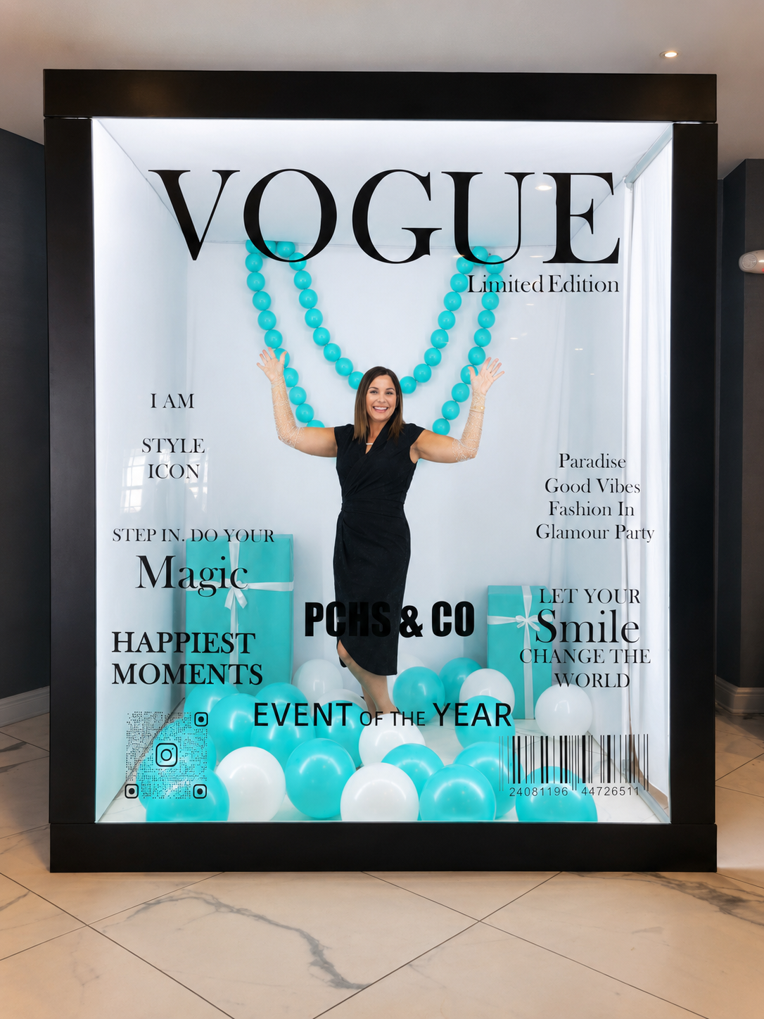 A woman standing inside a glass display window decorated with blue and white balloons, large blue bead necklaces, and gift boxes, with various motivational and fashion-related phrases and social media icons on the glass. Chicago events decor photo bo