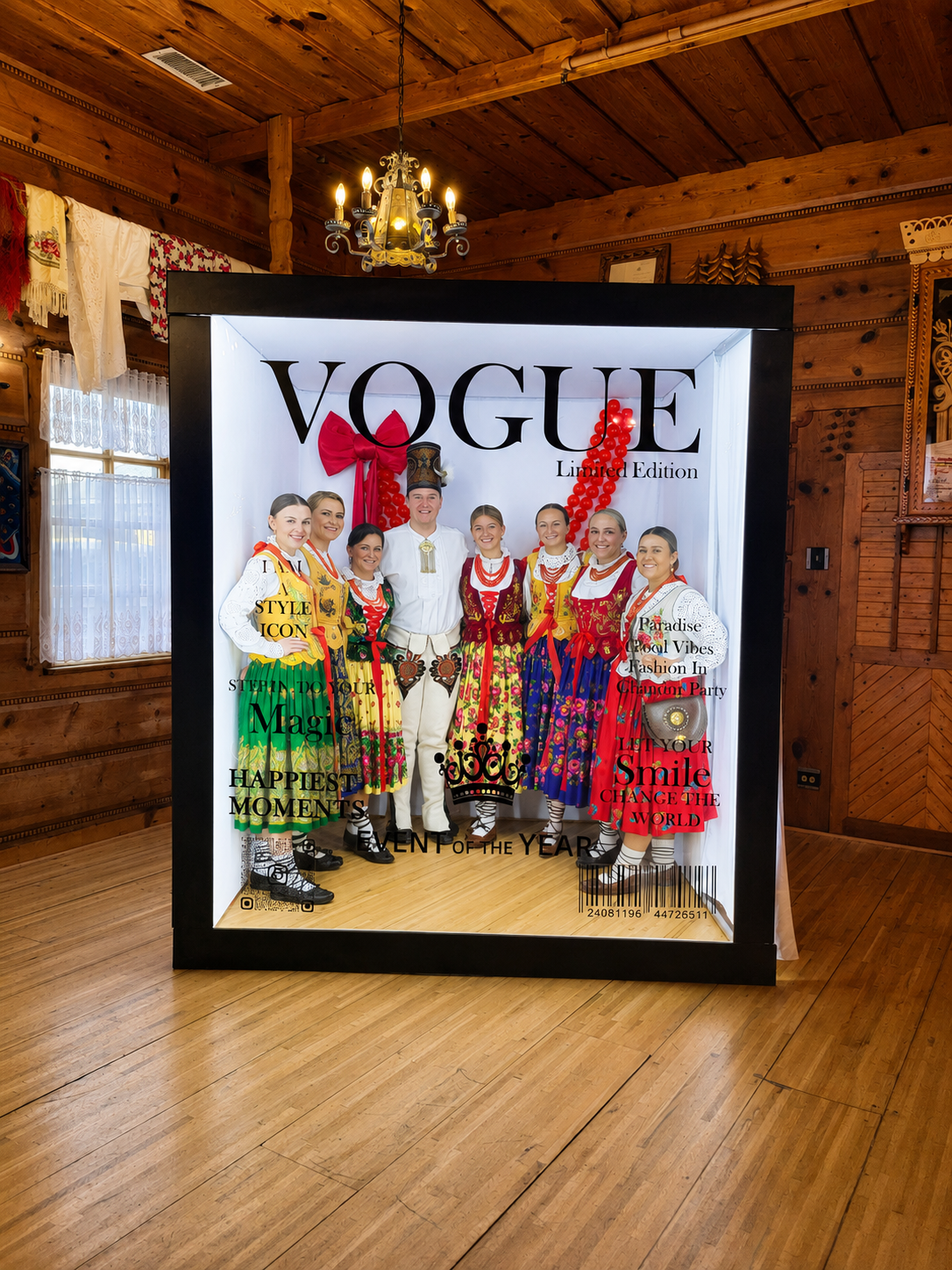A group of people dressed in traditional colorful folk costumes inside a display box with a Vogue logo. The display features a large red bow and text celebrating style, magic, happiness, and cultural moments. Chicago events decor photo booth rental