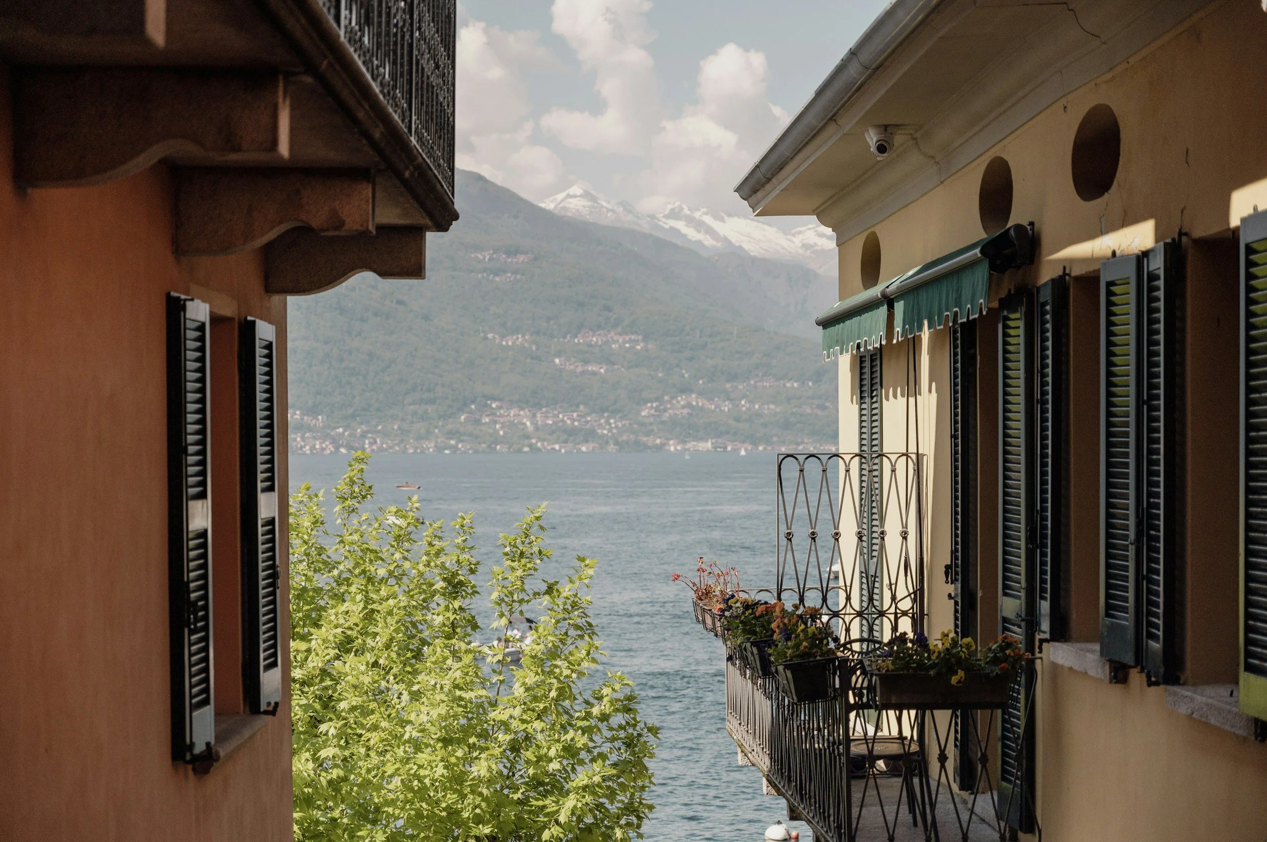 Vista di un lago tra le montagne viste da una via di un edificio, con balcone e fiori sul balcone.