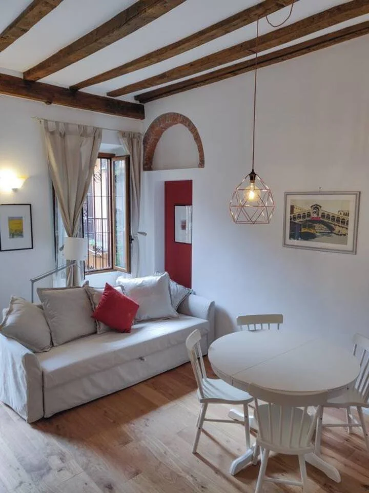 A bright living room with large window, red armchair, white cabinet, and wall art, featuring natural light and modern decor.