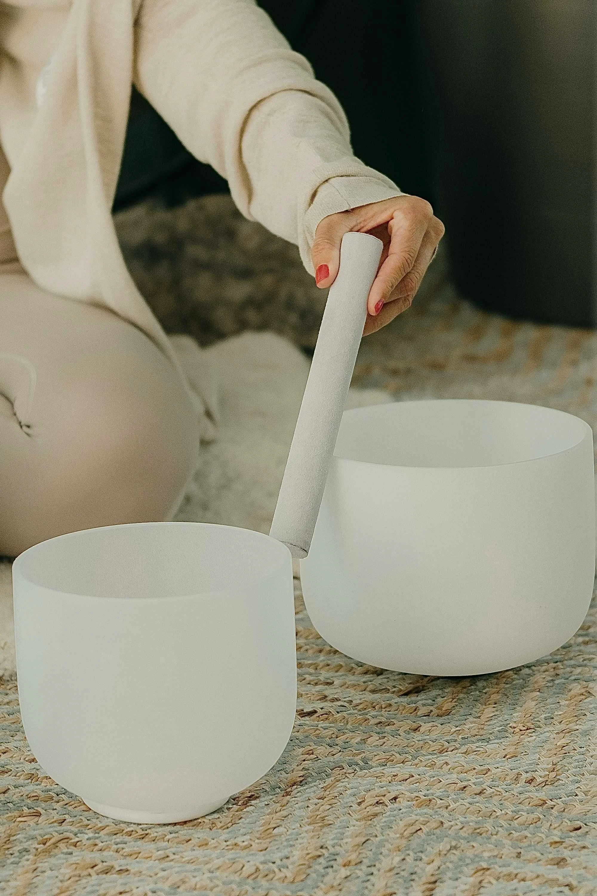 Close-up of a person's hand holding a piece of white paper above three small white bowls on a textured rug.