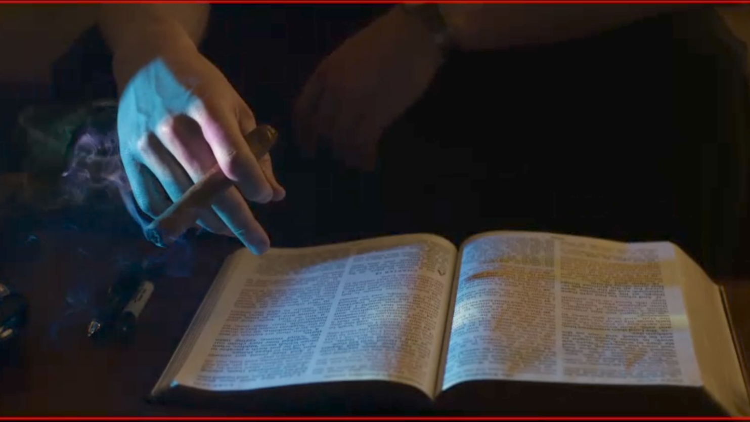 A person with a ring on their finger is using their finger to turn the pages of an open book illuminated by a blue light, with some scattered batteries on the table.