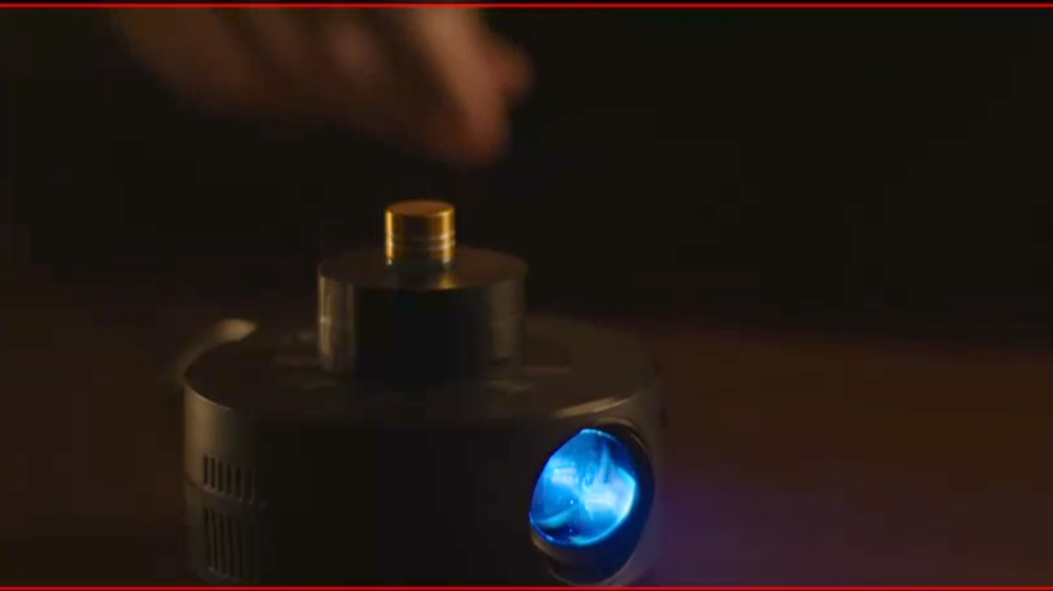Close-up of a small device with a glowing blue light, with a person's hand above it in a dark setting.