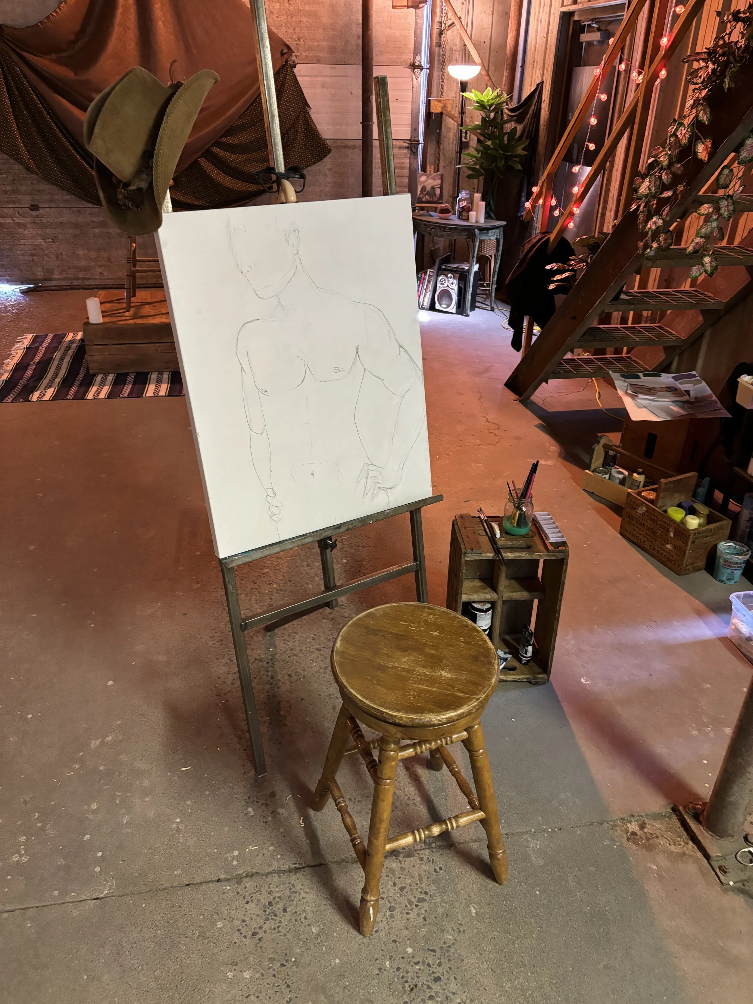 An art studio with a wooden staircase, a white canvas with a sketch of a nude woman, a stool, and various art supplies and decorations.