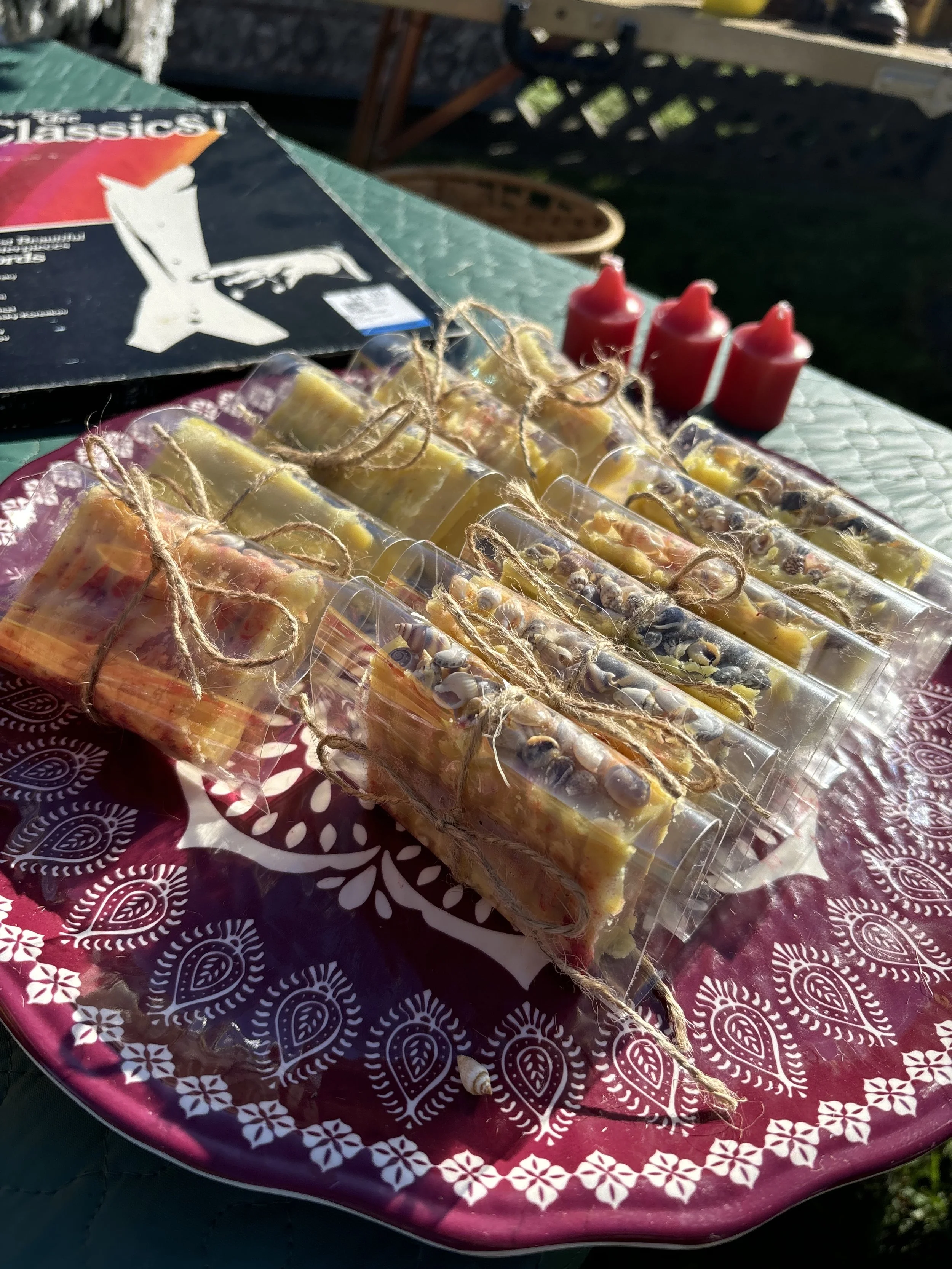 Colorful soap bars tied with twine on a decorative tray, with red squeeze bottles in the background, and a magazine or booklet partially visible on a green surface.