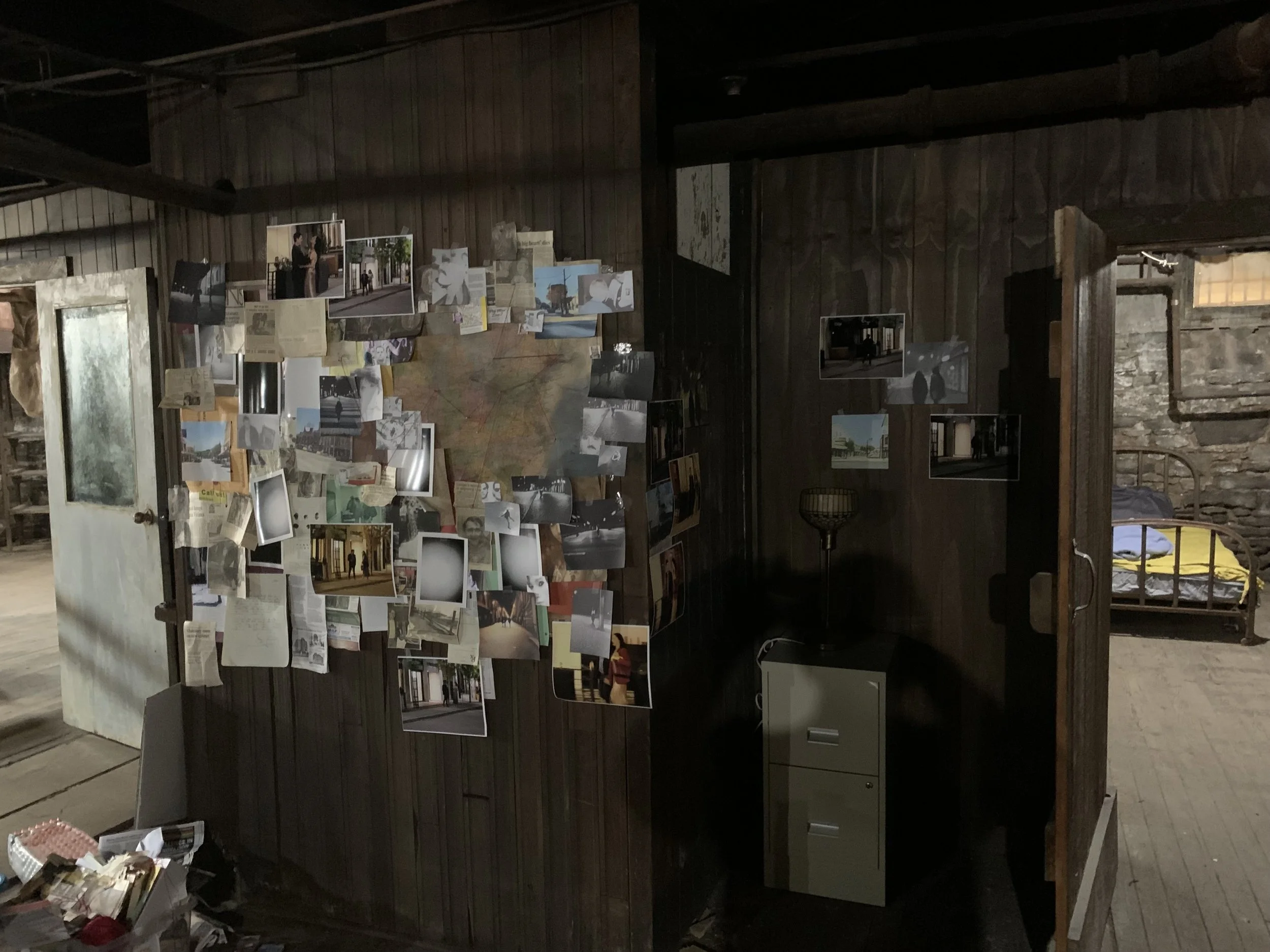 A dark room with wooden walls displaying photos and notes on a large board, and a stone fireplace on the right side.