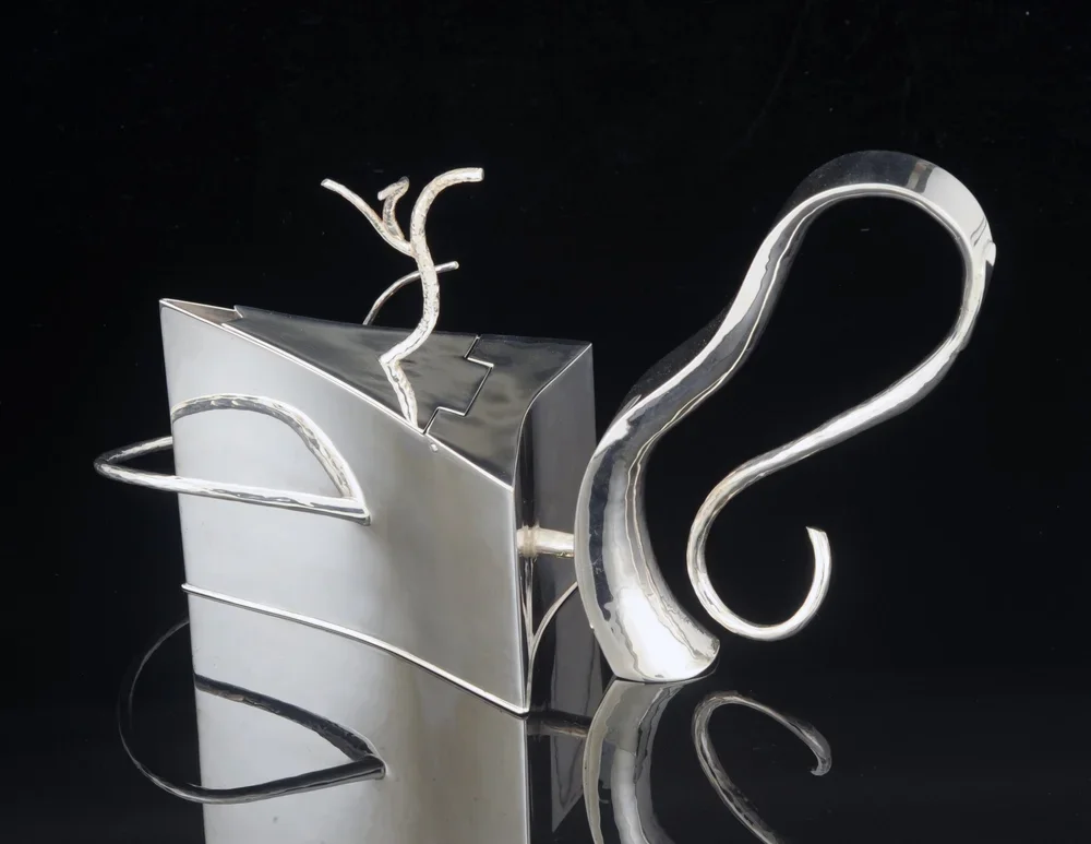 Teapot metal sculpture with abstract shapes and curved elements on a black background.