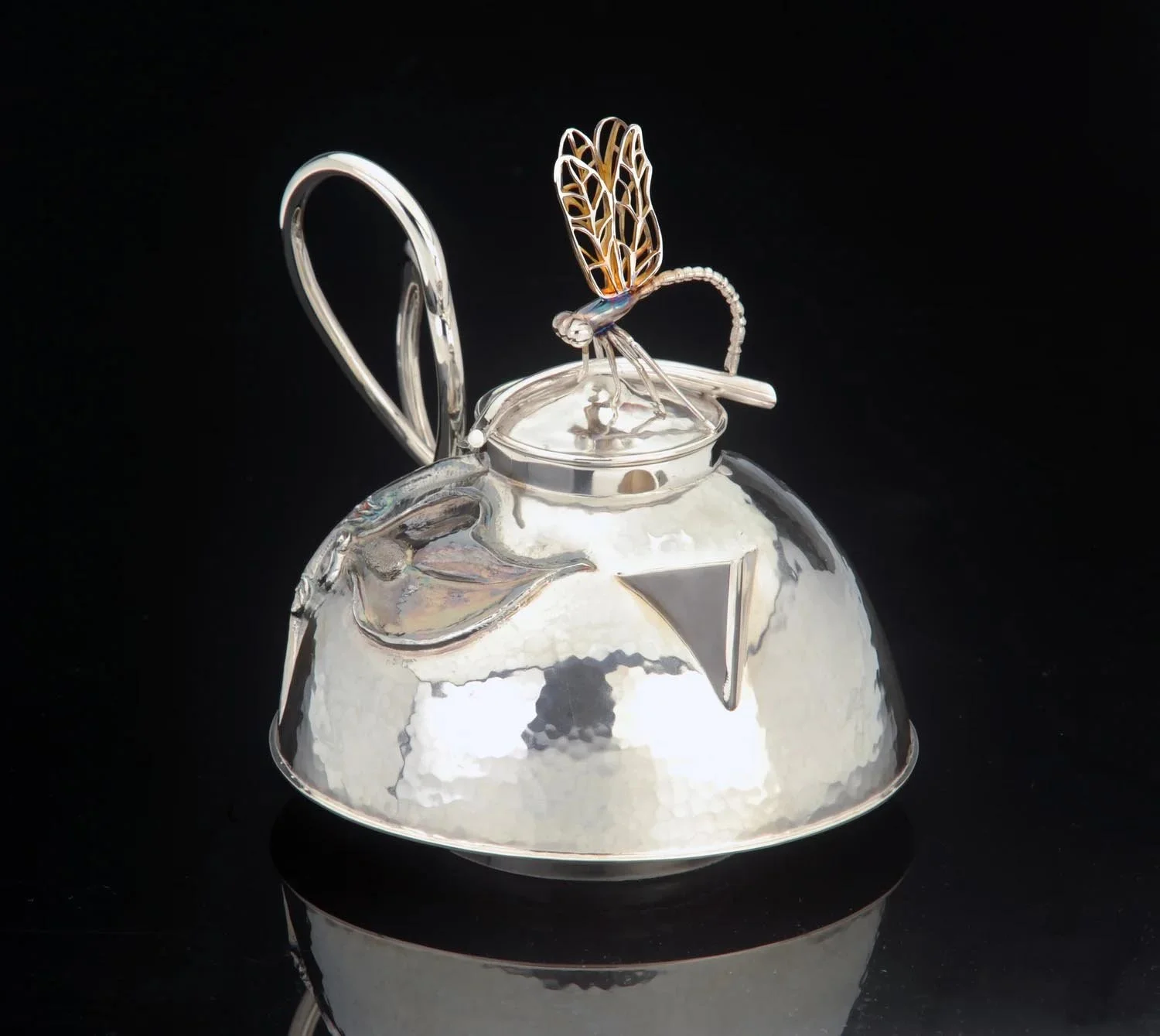 Silver teapot with a decorative butterfly-shaped ornament on the lid, set against a black background.