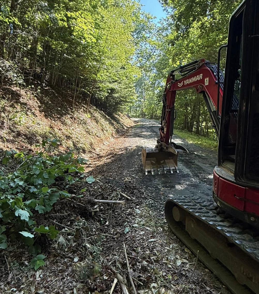 Excavator performing roadway drainage improvements and gravel road restoration by M&S Land Management in Western North Carolina.