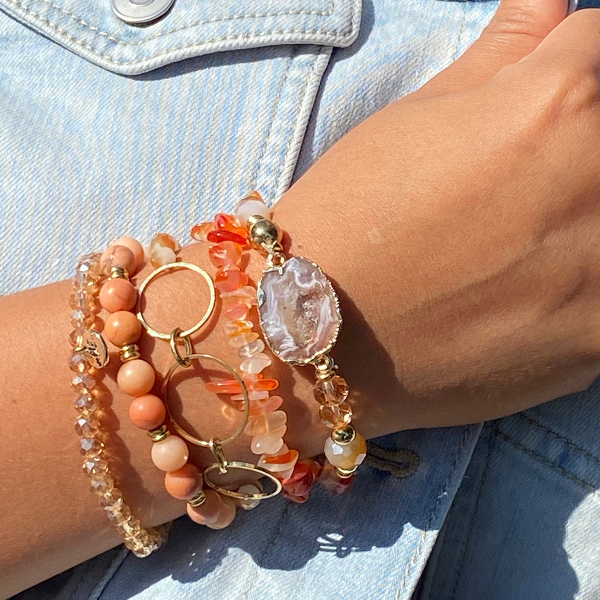 Close-up of natural stone stackable bracelets worn on a person's wrist, with a denim jacket and gold ring visible in the background.