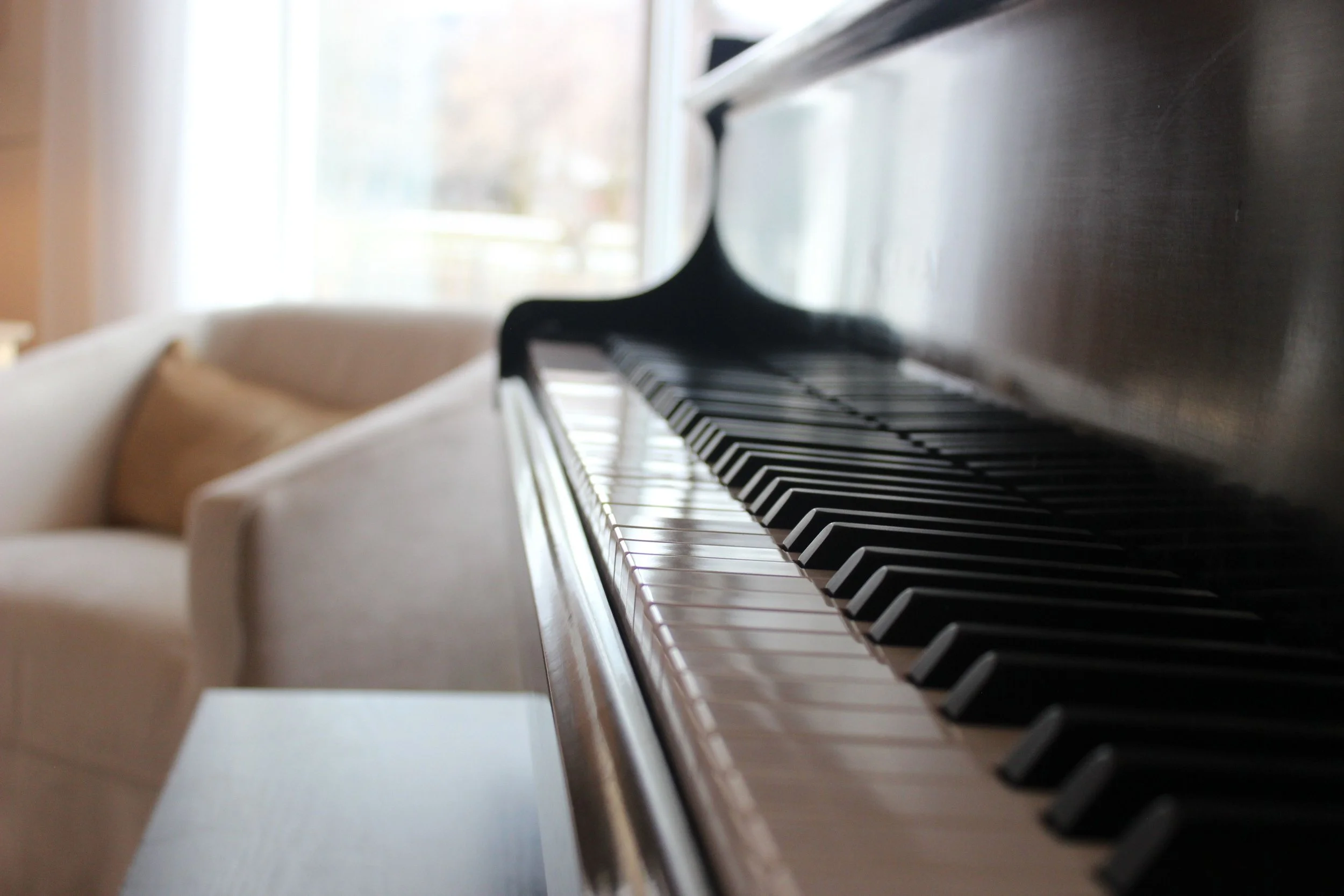 Close-up of a piano keyboard with black and white keys, with sunlight coming through a window in the background.