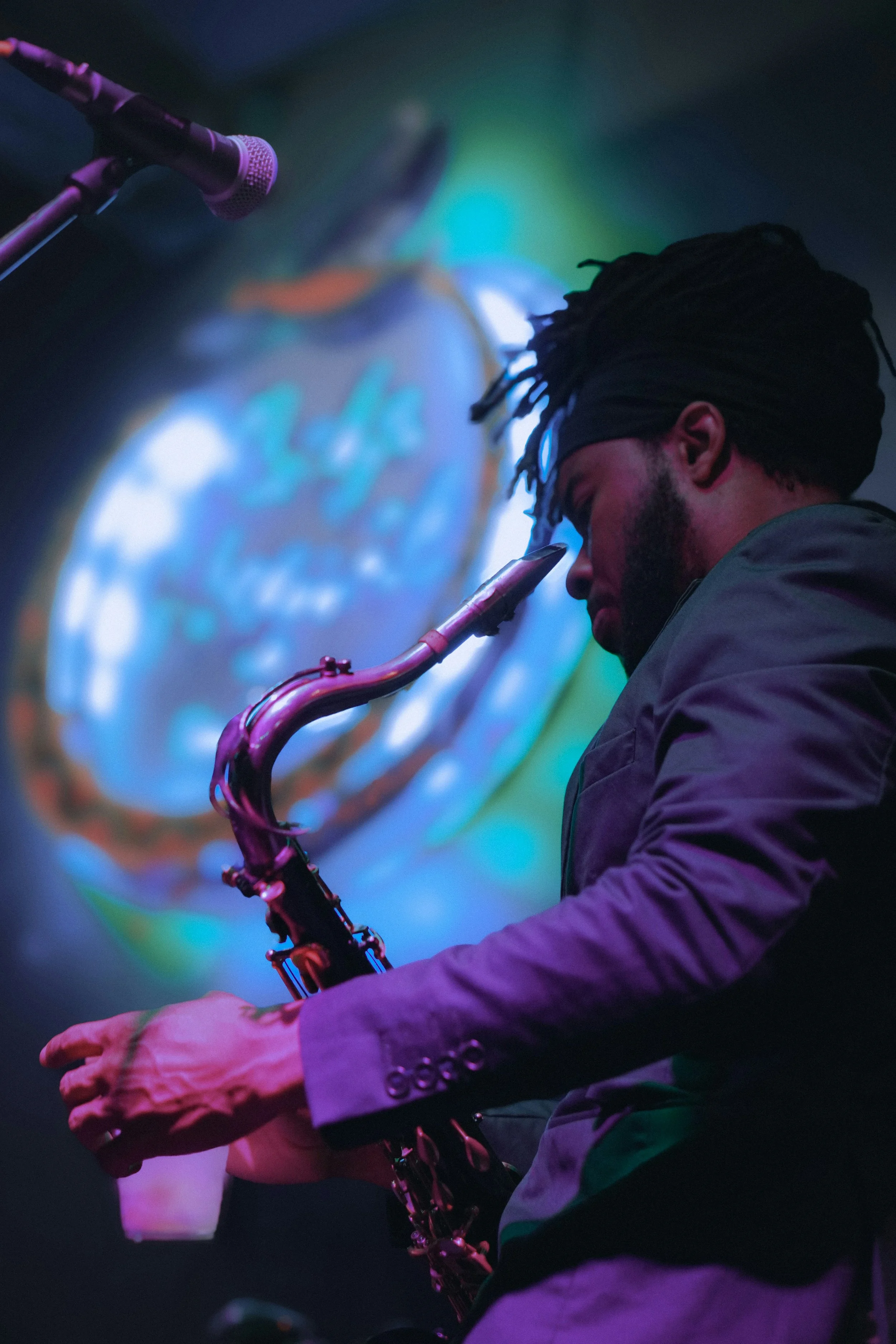 A musician playing a saxophone on stage with colorful blurred lights in the background.