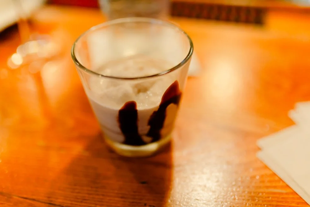 A glass filled with a light-colored creamy beverage, garnished with drizzles of chocolate syrup on the inside.