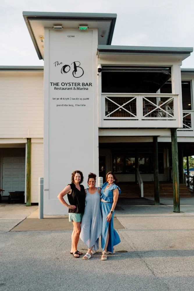 Three women standing in front of The Oyster Bar restaurant in Perdido Key, Florida, smiling at the camera.