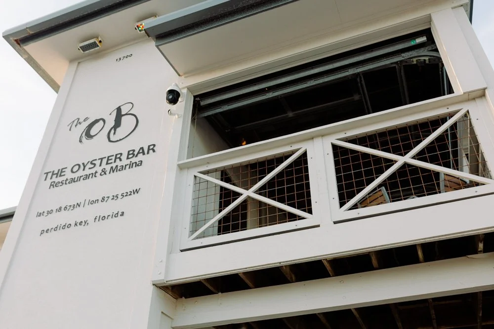 White building with signage reading 'The OB Oyster Bar Restaurant & Marina,' located in Perdido Key, Florida, with a partially enclosed balcony.
