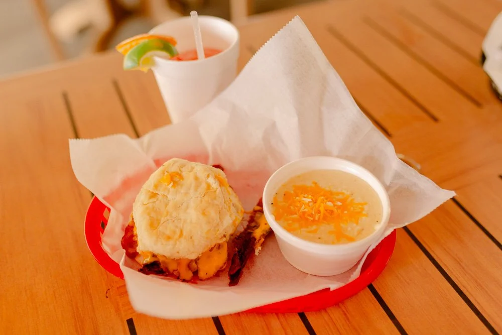 Tray with a biscuit, a bowl of soup with shredded cheese, and a cup of cocktail with lime and garnish on a wooden table.